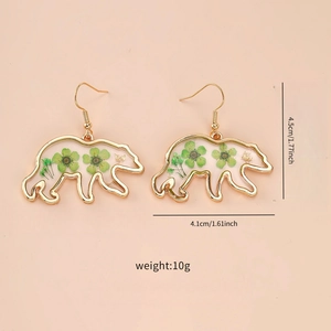 Detail view of bear shaped resin earrings with green dried flowers and gold foil accents