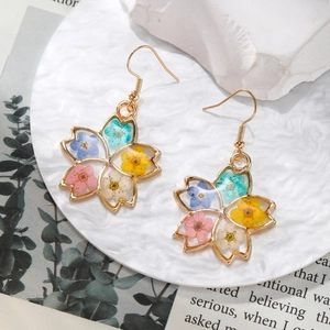 Colorful dried flower earrings in gold metal frame on a white ceramic plate