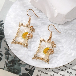 Close-up of gold rectangle drop earrings with white dried daisy flowers in resin