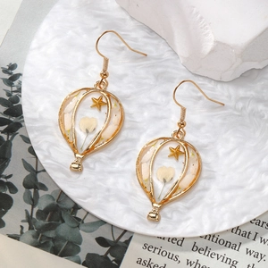 Detailed close-up of handmade gold hot air balloon earrings with white dried flowers