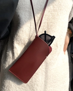 Detail of dark red leather glasses case with stitching on a model wearing a white sweater