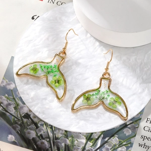 Close-up of golden whale tail earrings with real green dried flowers in clear resin