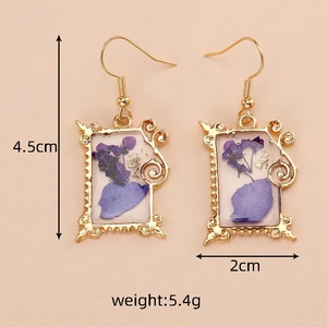 Detail view of handmade gold rectangular frame earrings with purple dried flowers and gold foil