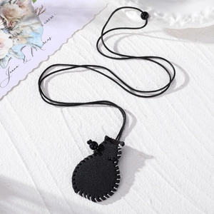 Detail of black leather pouch necklace with white stitching and woven cord on white surface