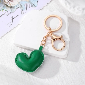 Detailed close-up of a green leather heart keychain with fine stitching and gold clasp
