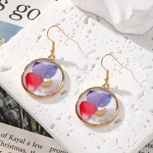 Close-up of golden round drop earrings featuring real purple dried flowers in resin