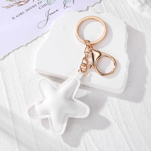 Detail of white star-shaped leather keychain with gold lobster clasp on stone tray