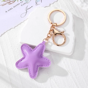 Detailed close-up of a purple star leather keychain with gold metal clasp on white stone