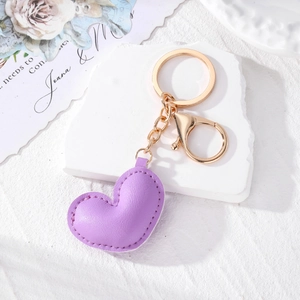 Minimalist lavender purple leather heart keychain with golden hardware on a white stone base