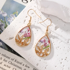 Close-up of teardrop resin earrings with purple dried flowers and gold leaf details