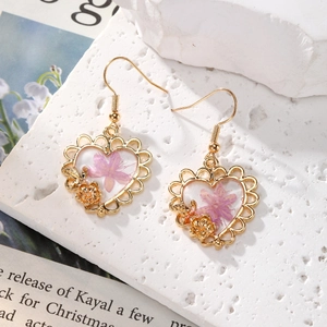 Elegant purple dried flowers in heart-shaped resin gold drop earrings on stone background