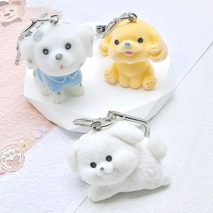 Three cute flocked dog figurines as keychains displayed on white geometric stands