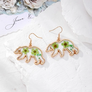 Detailed macro view of golden bear earrings with embedded green dried flowers