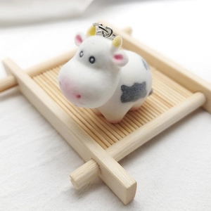 Close-up of a cute flocked cow keychain with pink details on a bamboo tray