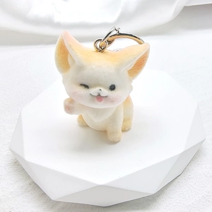 Close-up of a cute flocked fennec fox keychain with pink ears on a white platform