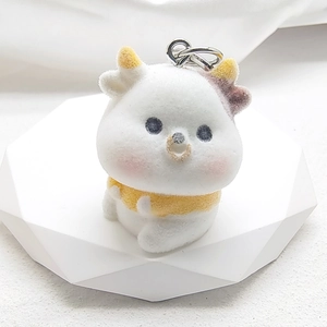 Close-up of white flocked animal keychain with yellow scarf on geometric stand