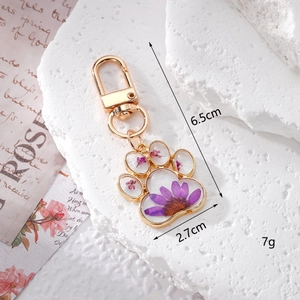 Detail of cute cat paw keychain with purple daisy dried flowers in golden frame