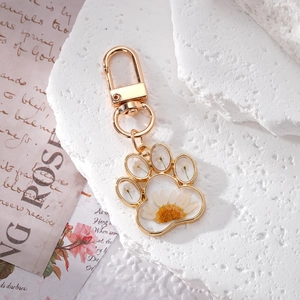 Macro detail of cat paw keychain with real daisy flowers and gold resin frame
