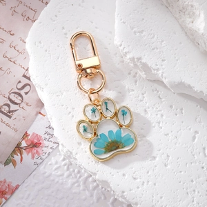 Cute cat paw keychain with blue dried flowers in resin and gold metal frame on white stone