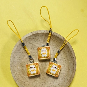 Set of three cute resin cat toast charms with yellow woven straps on a wooden tray