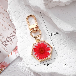 Detail view of hexagonal daisy resin keychain with real red flower and gold metal clip