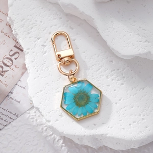 Close-up of hexagonal gold keychain with real blue dried daisy encased in clear resin
