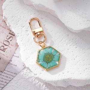 Detail of a golden hexagonal daisy resin keychain with a real dried flower in blue-green