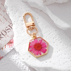 Detailed macro view of a hexagonal gold pendant featuring a real pink daisy in resin