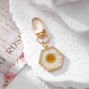 Close-up of hexagonal gold keychain featuring real white daisy pressed in clear resin