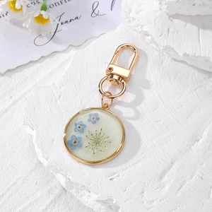 Detail of round resin daisy keychain with dried blue flowers and golden lobster clasp