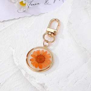 Detailed macro view of an orange dried daisy flower preserved in a round resin keychain pendant