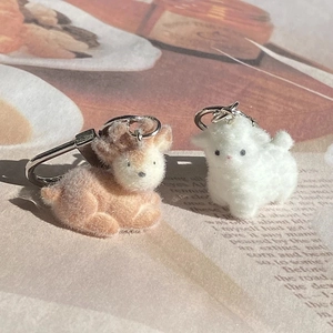 Cute brown and white flocked alpaca plush keychains with silver metal clasps on magazine