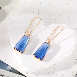 Detailed macro view of geometric blue trapezoid crystal earrings with golden hooks on white stone