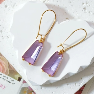Macro shot of faceted purple glass earrings on a white heart-shaped stone tray