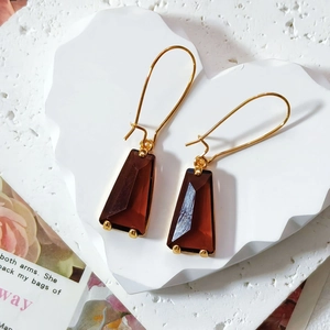 Detail view of brown trapezoid glass earrings with golden metal hooks on white stone