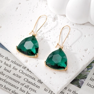 Close-up of dark green geometric crystal earrings with gold hooks on a marble background