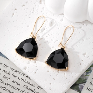 Detail of black geometric crystal earrings with gold trim on white textured background