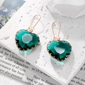 Detalle de pendientes de cristal verde esmeralda con forma de corazón y gancho dorado