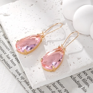 Detail of pink crystal teardrop earrings with gold four-prong setting on stone surface
