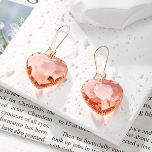 Elegantes pendientes de corazón de cristal rosa con garras doradas sobre piedra blanca