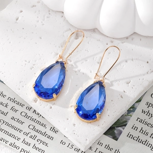 Detail of blue teardrop faceted crystal earrings with gold claw setting on textured surface