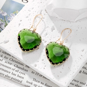 Detalle de pendientes de cristal verde en forma de corazón con borde dorado en bandeja
