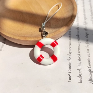 Miniature red and white lifebuoy charm with hanging cord on a vintage aesthetic background