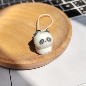 Cute panda plush keychain with pink elastic strap on a wooden tray for bags and keys