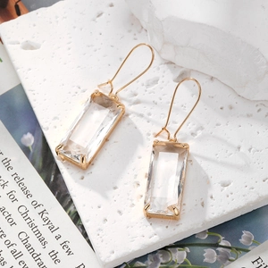 Détail de boucles d'oreilles en cristal avec crochets dorés sur fond blanc texturé