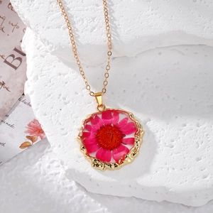 Detail of pink dried daisy in irregular gold frame necklace on natural stone