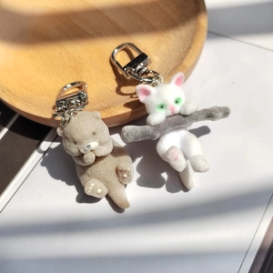 Détail de porte-clés loutre et chat floqués sur un plateau en bois avec attaches argent
