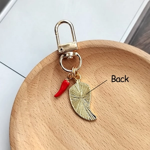 Golden keychain with 3D red chili pepper pendant and textured leaf charm on wooden tray