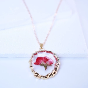 Macro detail of red dried rose inside transparent resin pendant with gold wavy frame