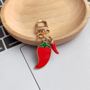 Close-up of a high-gloss red chili pendant keychain with green leaves and gold clasp